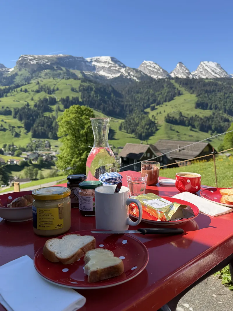 原图：红色餐桌上的早餐，前景盘中放着面包片，背景是雪山草坡