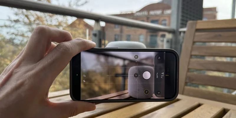 手持 iPhone 拍摄 HomePod mini 的相机界面,显示光圈与快门参数
