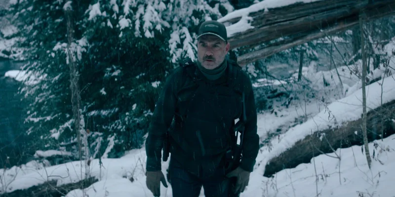 Nocturne 剧照：Liev Schreiber 饰演的 Jonah Lynn 在积雪森林中持枪行进