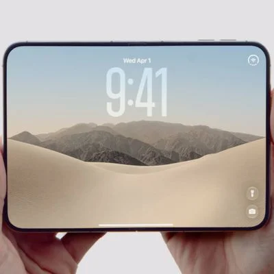 双手横向握持展开状态的 iPhone Duo，内屏显示锁屏时间 9:41 与沙漠山脉壁纸