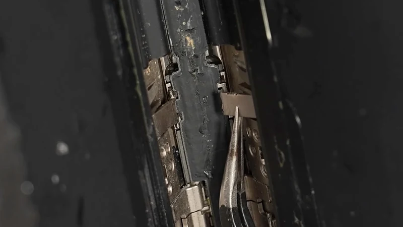 微距照片:iPhone Duo 铰链内部的金属支架与压板,右侧一根细长金属片已经断开并向外翘起,缝隙里能看到颗粒状碎屑和明显压痕