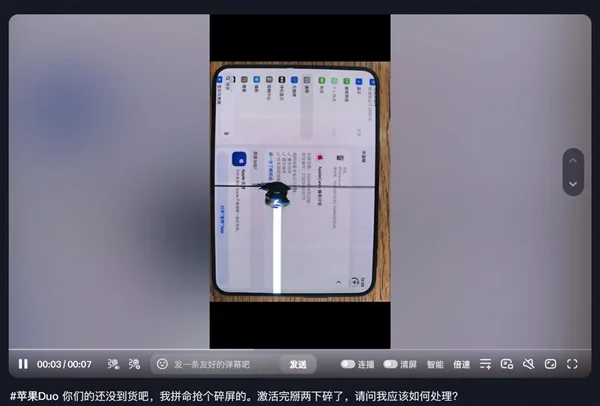 用户视频截图：两台 iPhone Duo 举在木纹桌面上，左侧那台的内屏中央有一道纵向白色亮线，画面底部是短视频平台的发送栏与手机电量图标