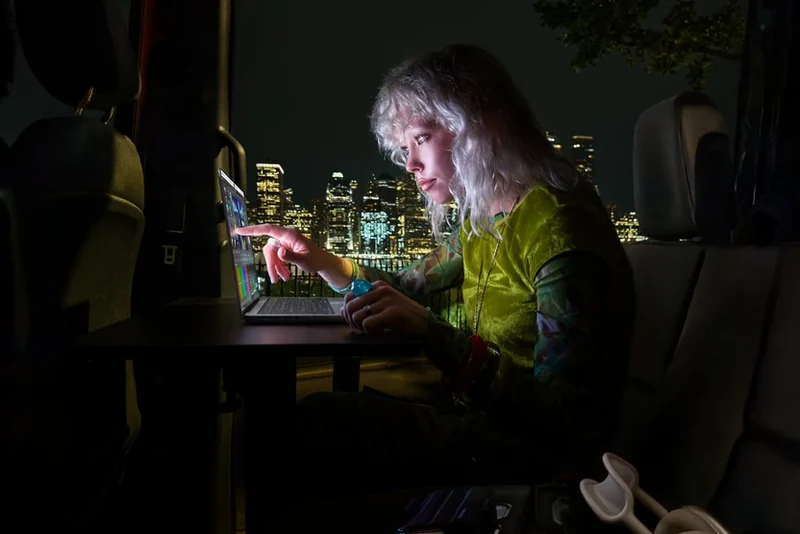 夜里坐在车内的人用手指点 MacBook Pro 屏幕,车窗外是亮着灯的城市高楼,屏幕的光照在人物侧脸上