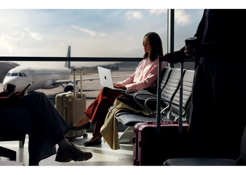 一名旅客在机场候机厅使用银色 MacBook Pro,窗外停着一架私人飞机