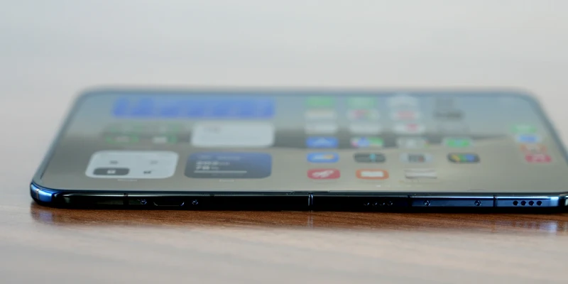 iPhone Duo 侧躺放置在木质桌面上,可见钛金属边框、侧边按钮与铰链接缝