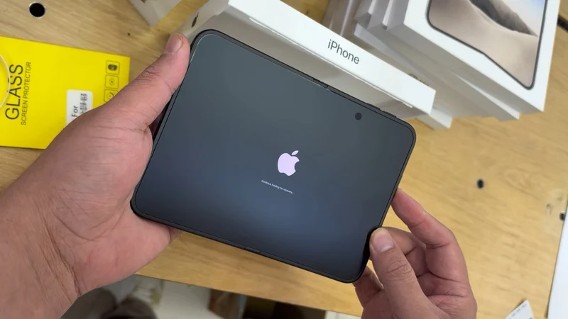 开箱视频画面：双手持展开状态的 iPhone Duo，内屏显示苹果 Logo 与正在连接到 iCloud 提示，一旁可见 iPhone 包装盒