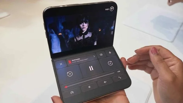 iPhone Duo 桌面模式实拍：机身折成约 90 度立在桌面，上半屏播放视频，下半屏显示播放控制项
