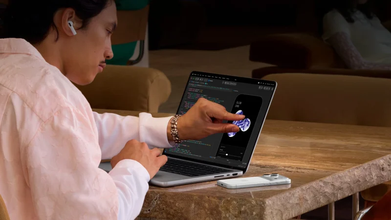 男子在MacBook Pro屏幕上的手机预览窗口用双指触控，旁边显示代码编辑界面