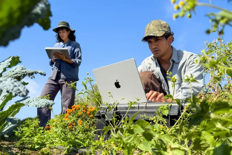 户外场景中一名创作者用手指触碰 MacBook Pro 屏幕,另一人站在远处看平板