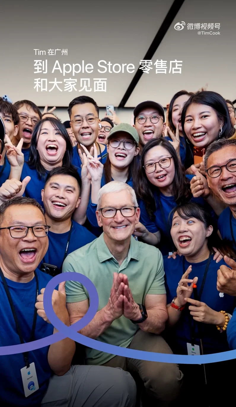 库克在 Apple Store 零售店与一群身穿蓝色工服的员工合影，众人举手欢呼