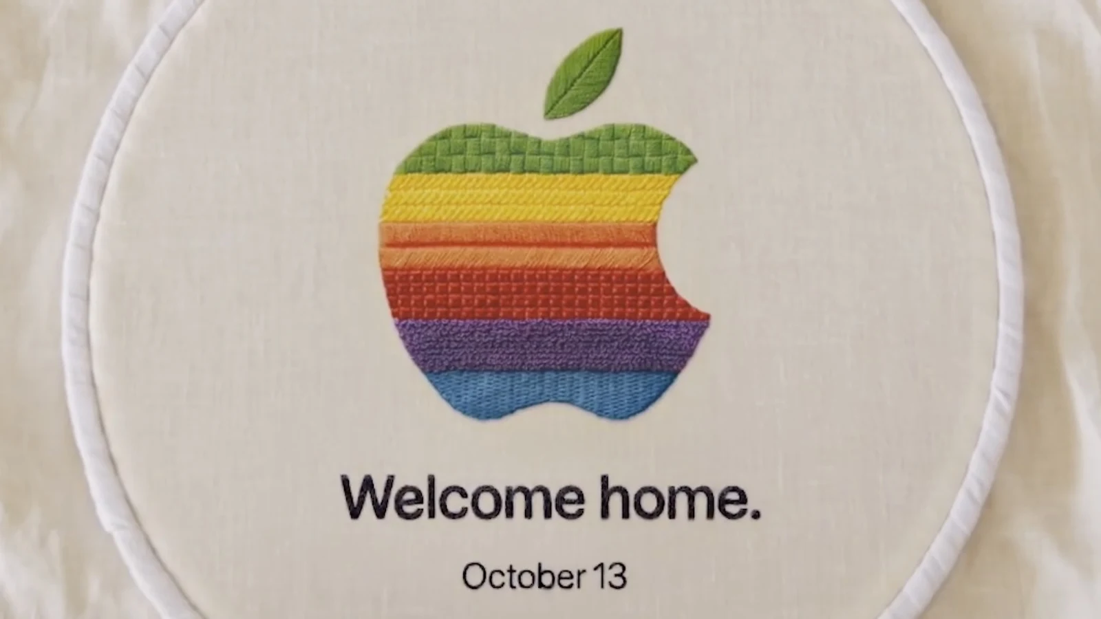 苹果官方 Welcome home 刺绣短片截帧,彩虹色苹果 logo 绣在布面上,下方写 Welcome home 与 October 13
